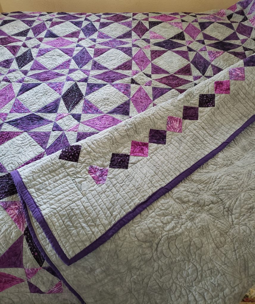 Folded multi-color handmade Storm At Sea quilt on a chair, showing vibrant cotton fabrics and quilt stitching