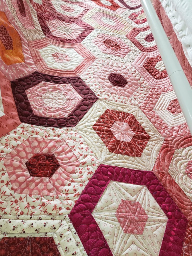Custom handmade quilt in cascading hexagon pattern with pink, red, and cream tones. Luxury bedding crafted with heirloom quality in the USA