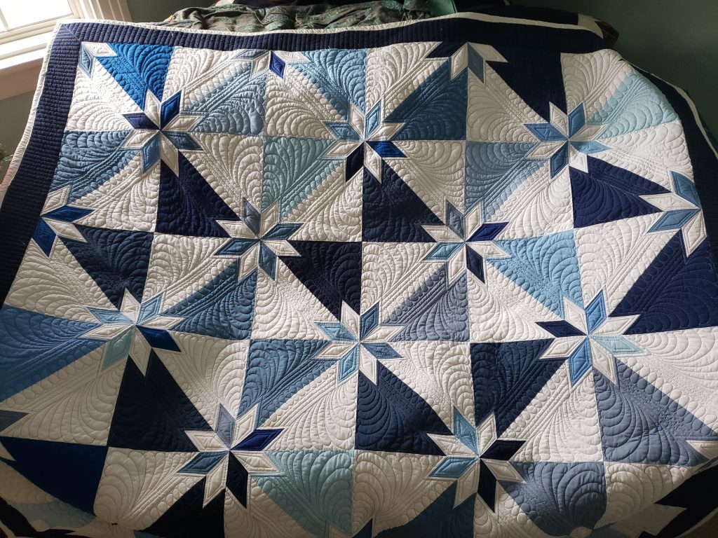 Handmade Quilts/ blue Hunter’s Star quilt draped across a Queen bed