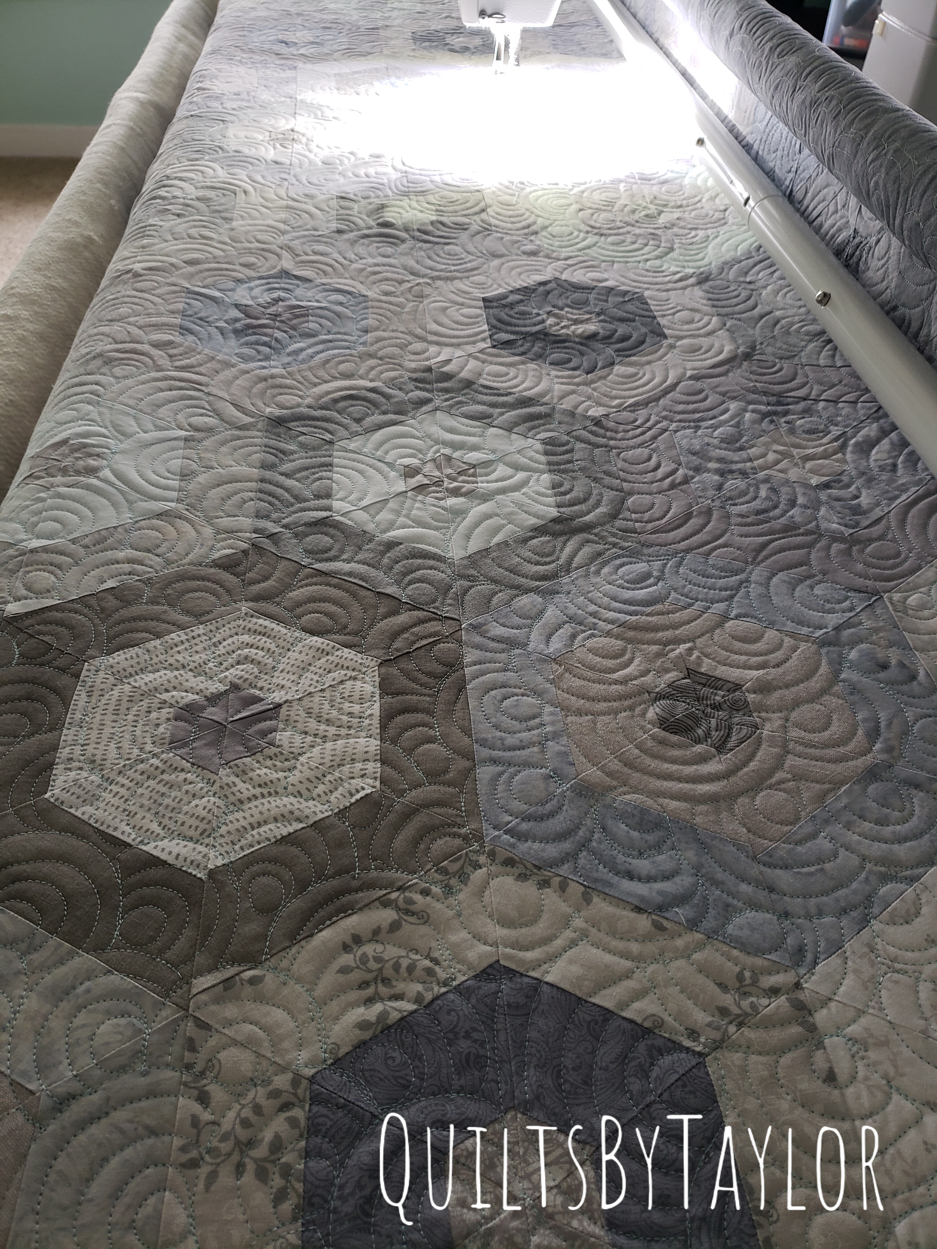 handmade neutral patchwork quilt being quilted on longarm machine with flowing quilting design