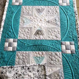Modern quilted star table runner in teal and cream fabrics featuring custom free motion quilting and textured peble quilting.